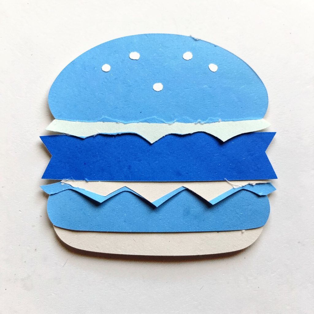 Collage di carta ritagliata con un burger vegetale a strati colorati, tonalità verdi, rosse e marroni, atmosfera vivace e appetitosa.